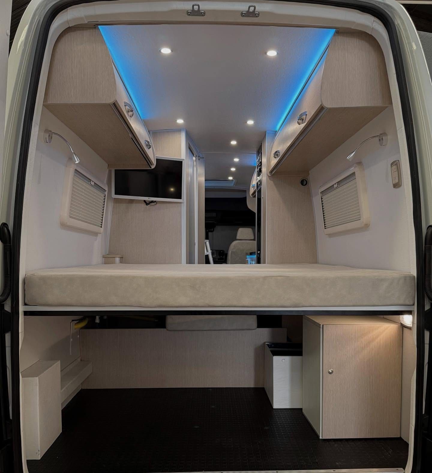 Cama transversal del fondo vista desde las puertas traseras, con TV, bauleras y luces LED