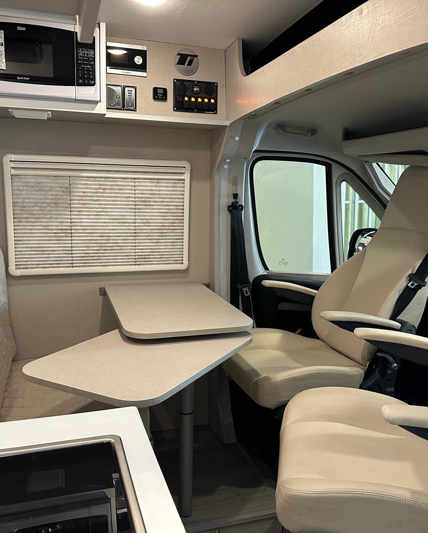 Comedor de la Citroën Jumper con mesa de dos hojas, butacas giratorias beige y microondas en el mueble alto