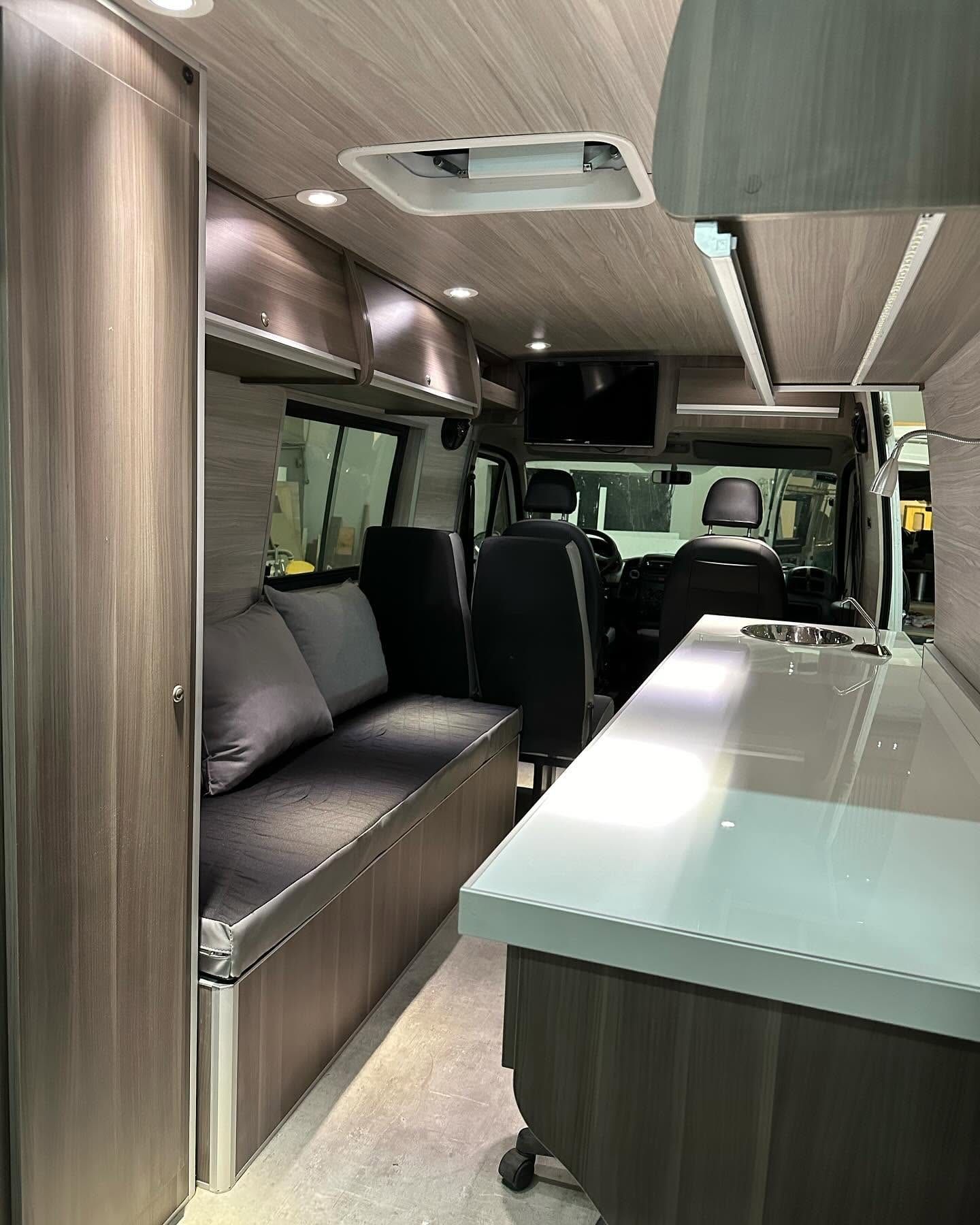 Sillón cama de la Fiat Ducato con almohadones grises, frente al plano de trabajo con bacha