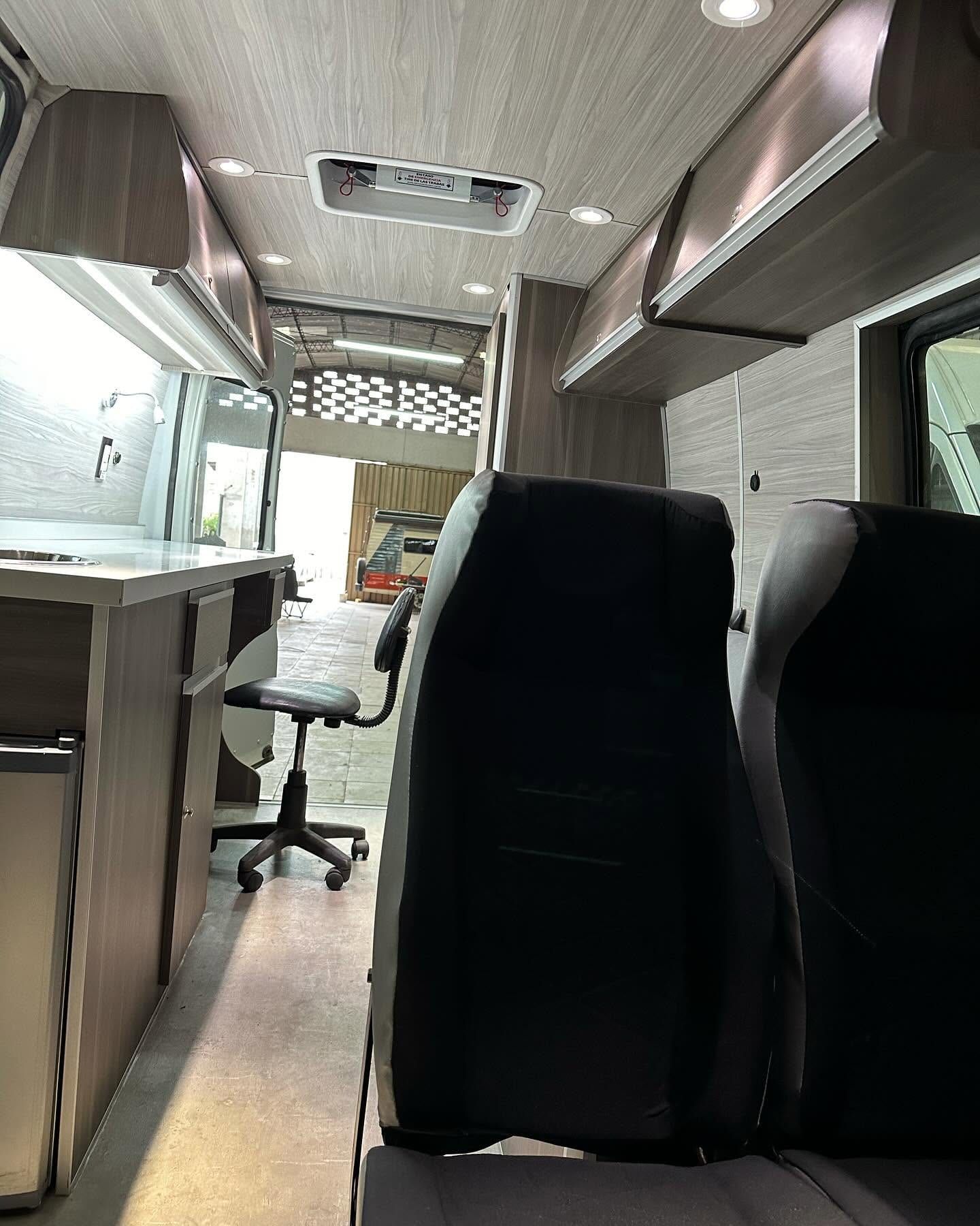 Interior de la Fiat Ducato visto desde el fondo, con la silla de oficina bajo la mesada y el portón del taller abierto