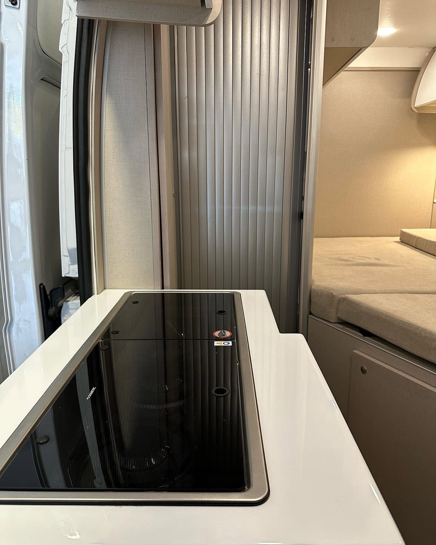 Mesada de cocina con la tapa de vidrio cerrada, junto a la puerta de persiana del baño