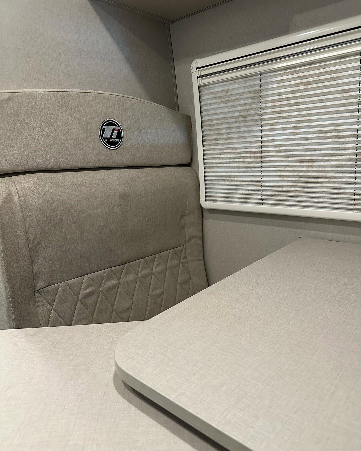 Butaca tapizada en beige con el logo Ti bordado, junto a la ventana con persiana plisada