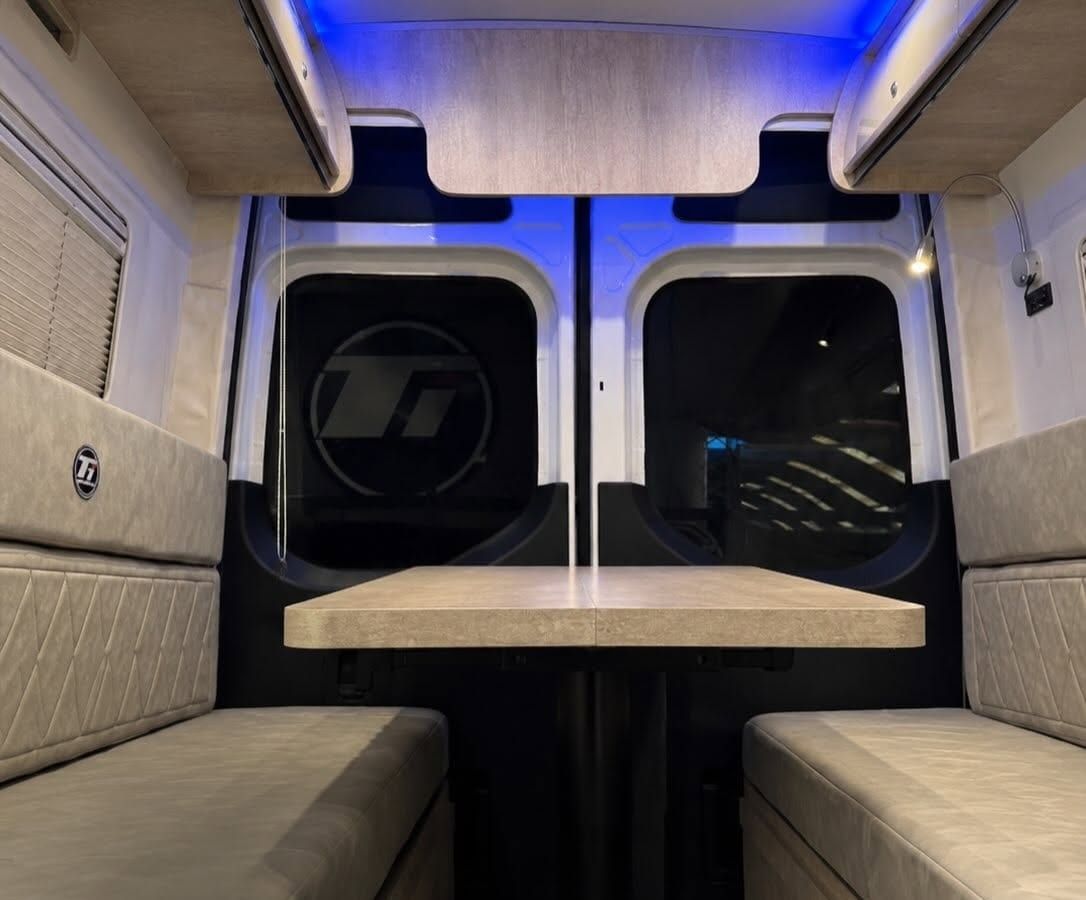 Comedor trasero con dos sillones enfrentados, mesa central y luz LED azul sobre las puertas traseras